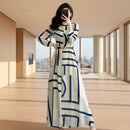 Woman in a long white dress with blue geometric patterns taking a mirror selfie in a modern room.