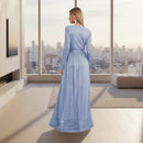 Woman wearing a long blue dress standing in a room with white walls and a small table.