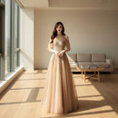 Woman in a beige evening gown with intricate detailing standing indoors.